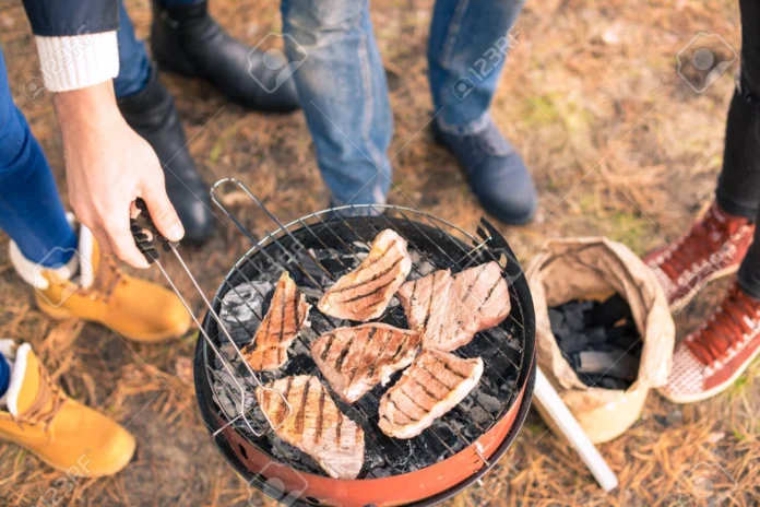 Personas cocinando carne en una parrilla al aire libre.